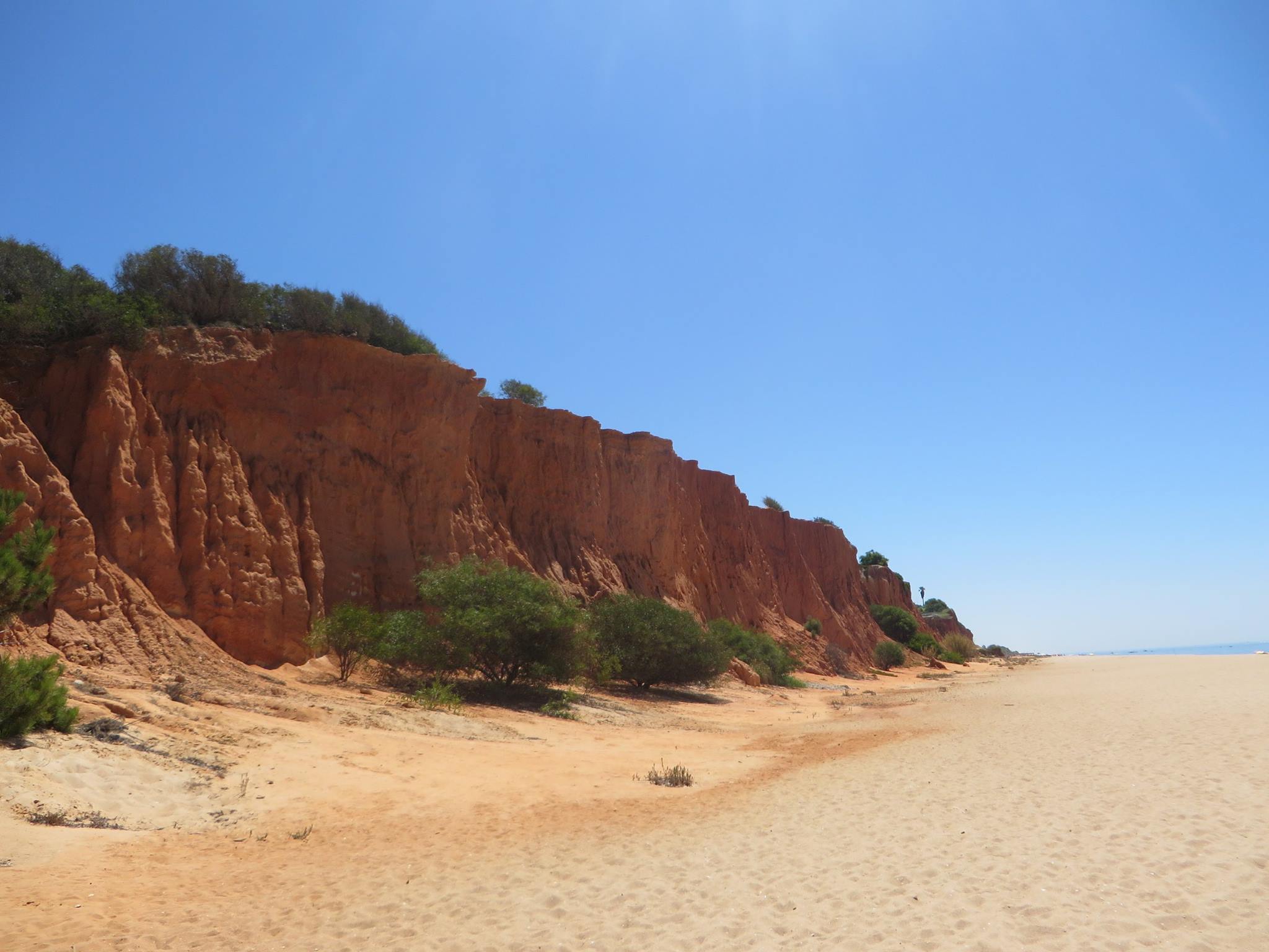 Dark red cliff edge overlooking a beautiful beach on a sunny day in the Algarve, Portugal.