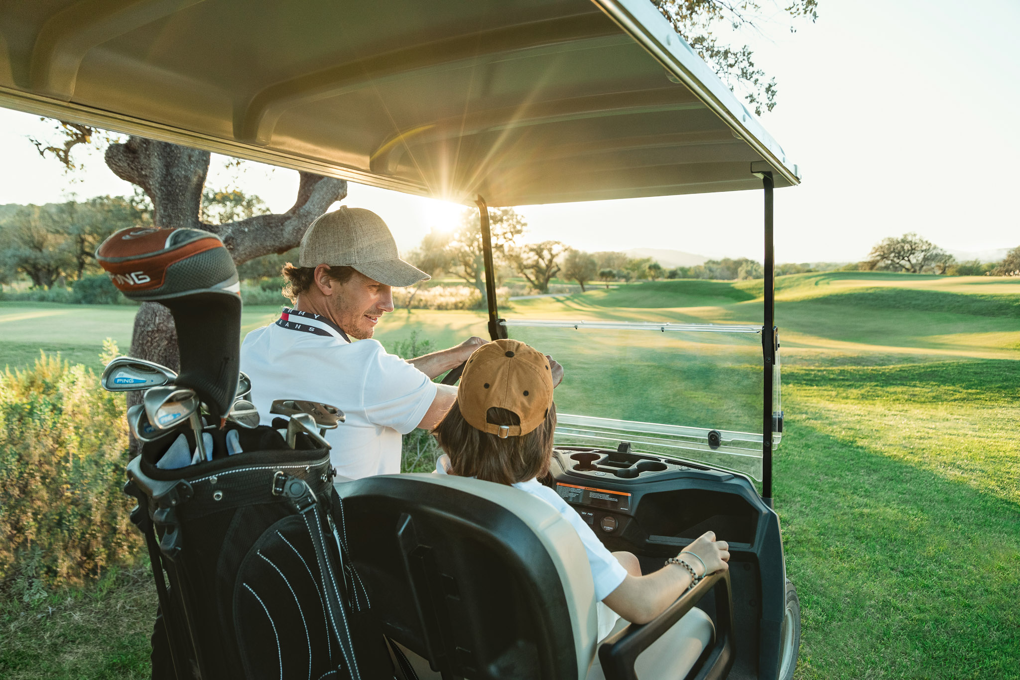 Father and son sat in a golf buggy together on a golf course.