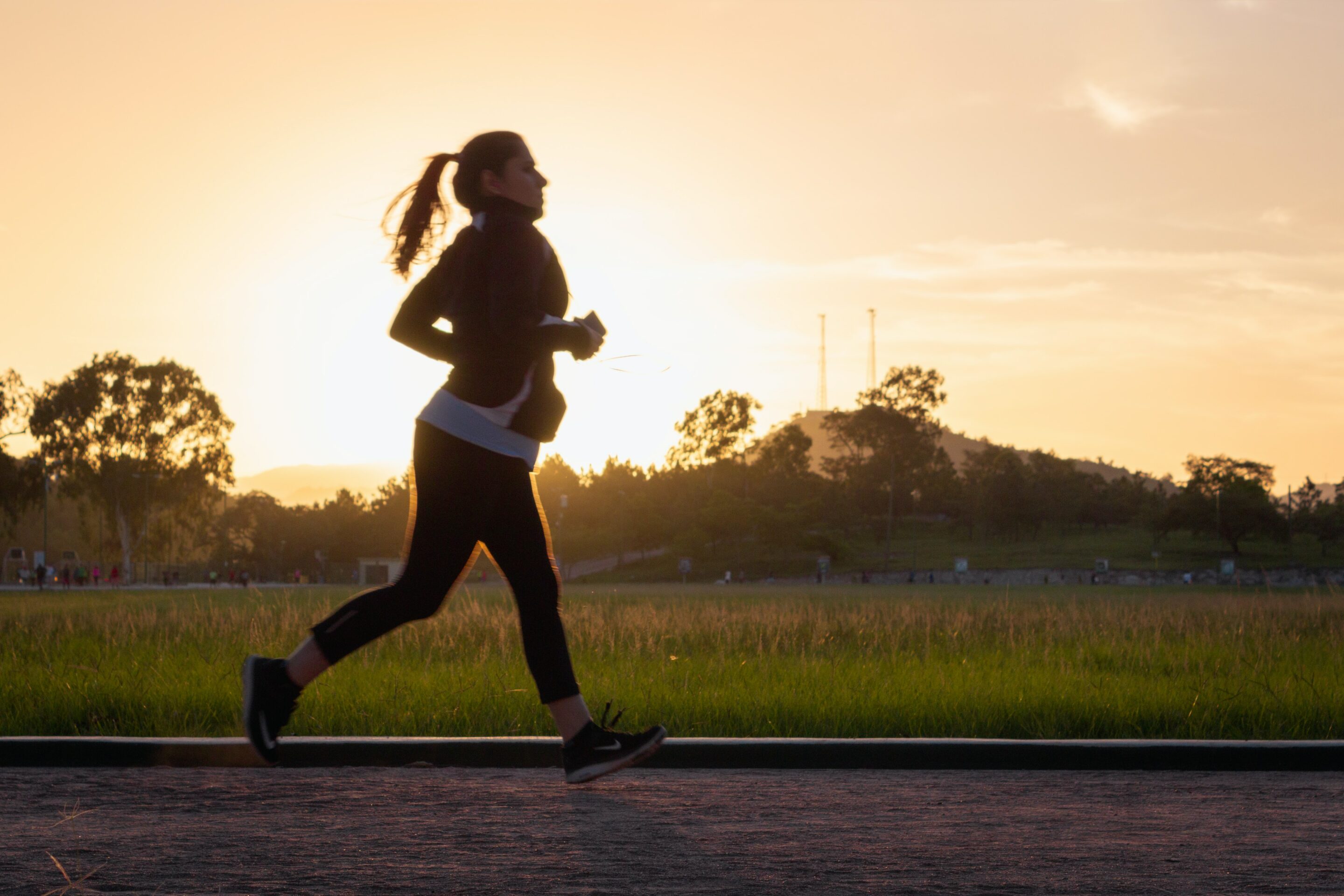 A woman is running on an athletics track while the sun is setting.